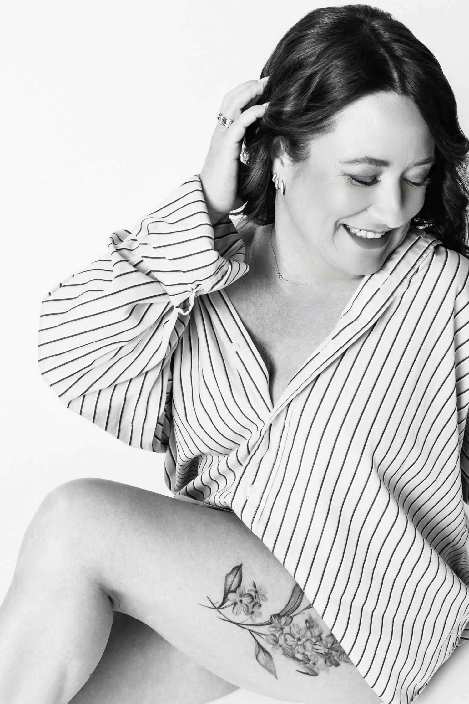 Black and white portrait of person in striped shirt laughing with floral leg tattoo.
