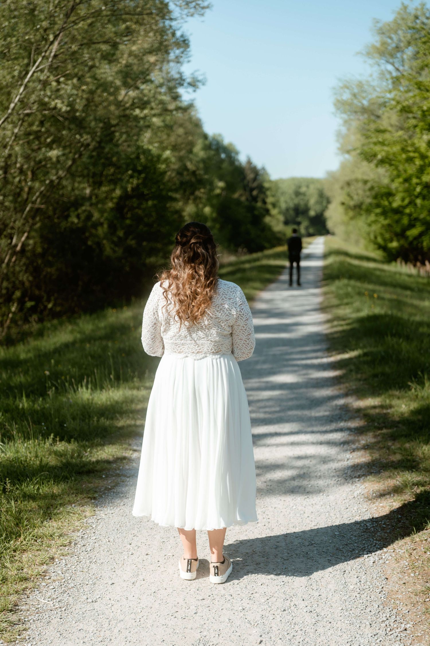 Braut nähert sich dem Bräutigam beim First Look auf einem Waldweg nahe dem Bodensee. Hochzeit Jacqueline & Clemens, fotografiert von NuMa