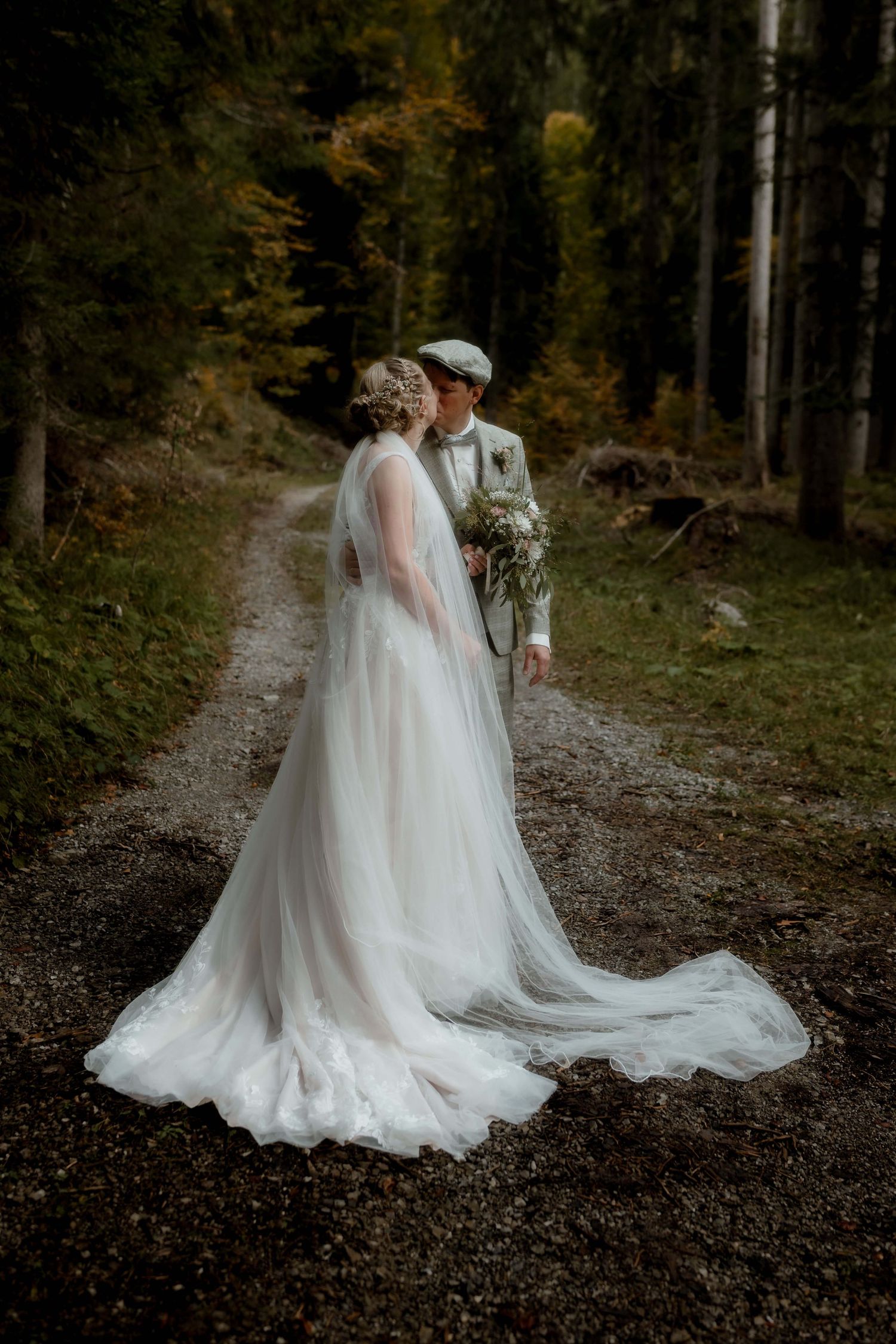 Brautpaar küsst sich auf einem Waldweg bei einer Boho-Hochzeit in Vorarlberg – NuMa Fotografie hält den Moment fest.