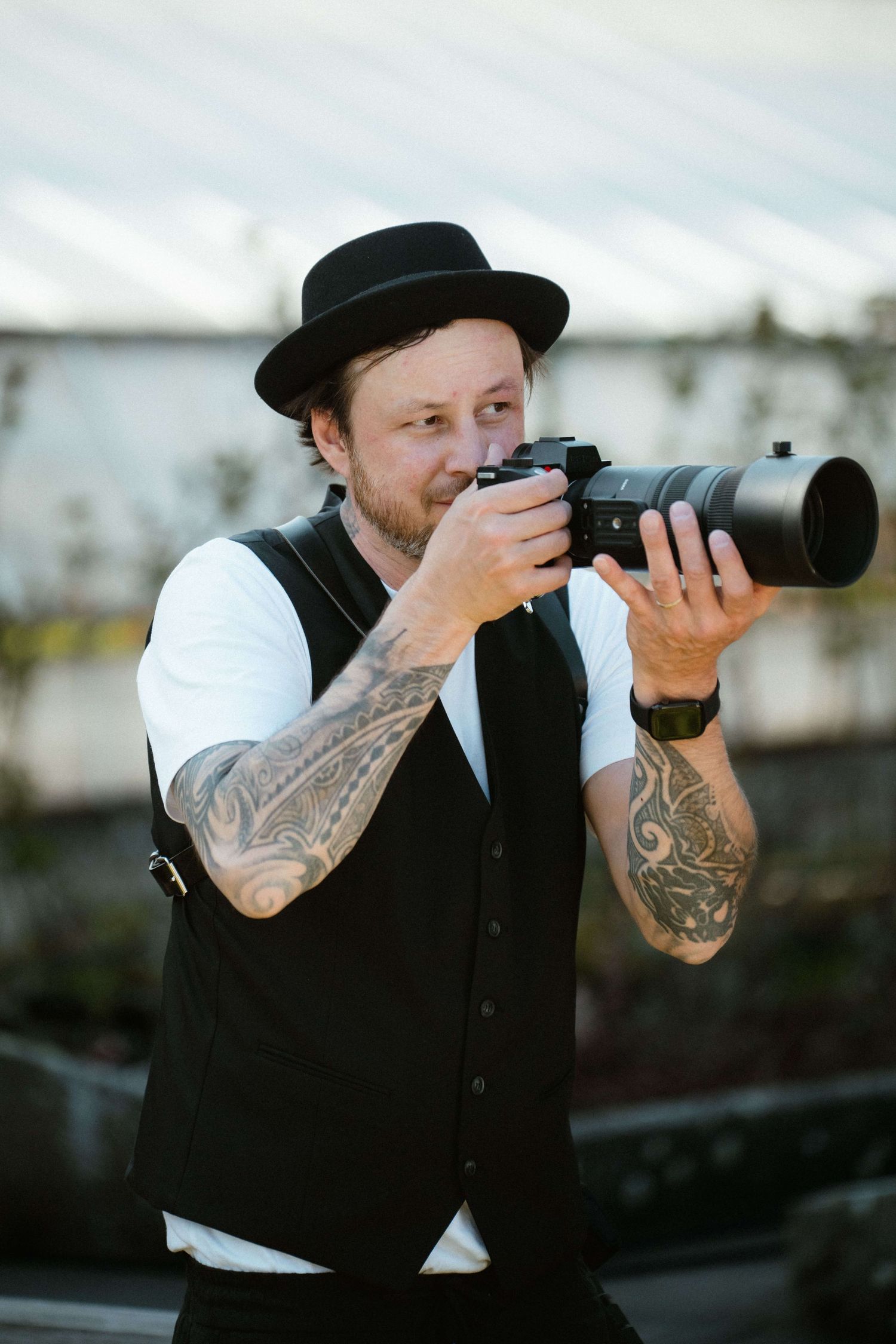 Portrait des Hochzeitsfotografen von NuMa Fotografie – mit Kamera, Tattoos und charakteristischem Hut.