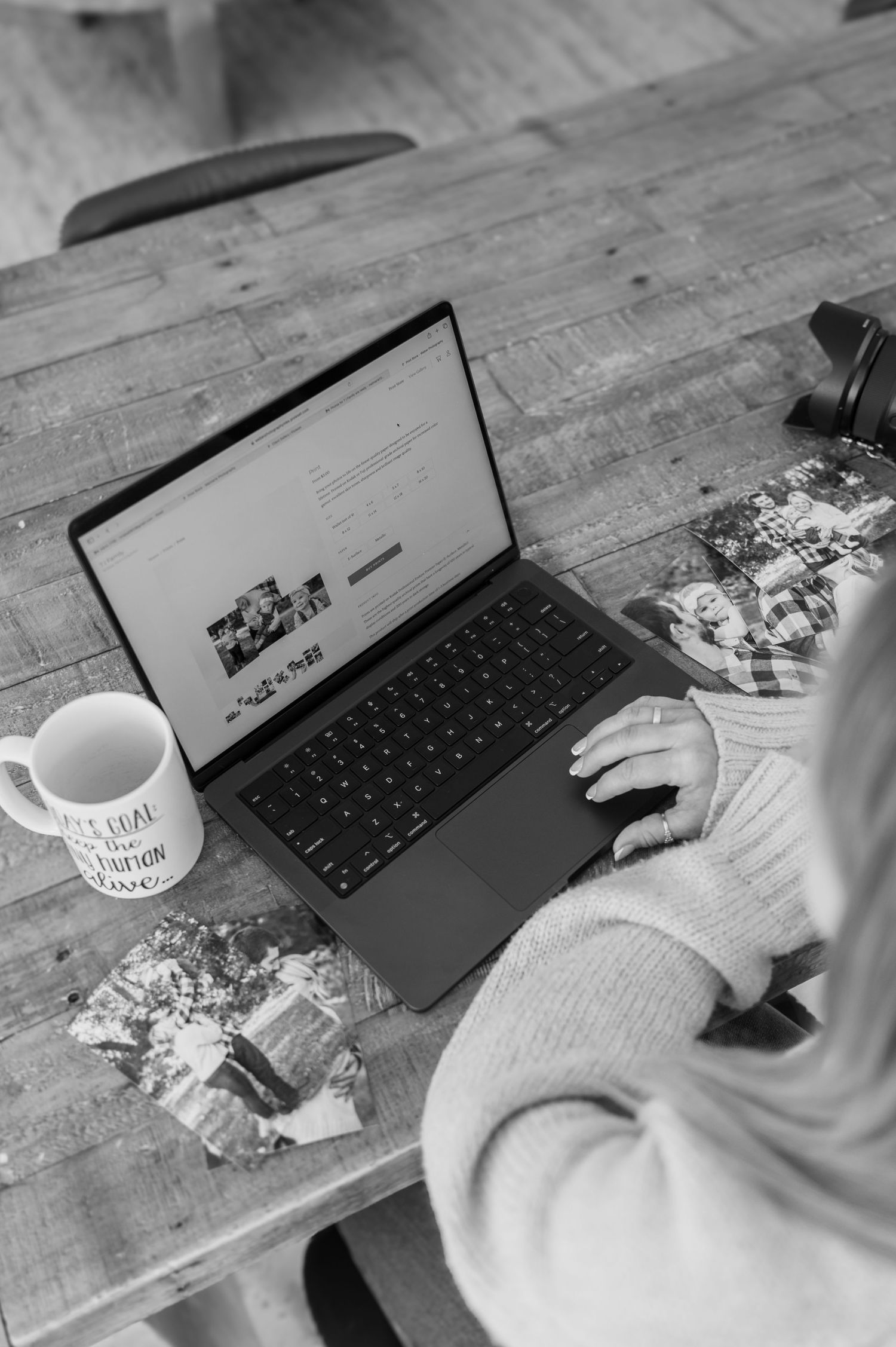 Person typing on laptop keyboard at rustic wooden desk with coffee cup next to it in black and white photography style.