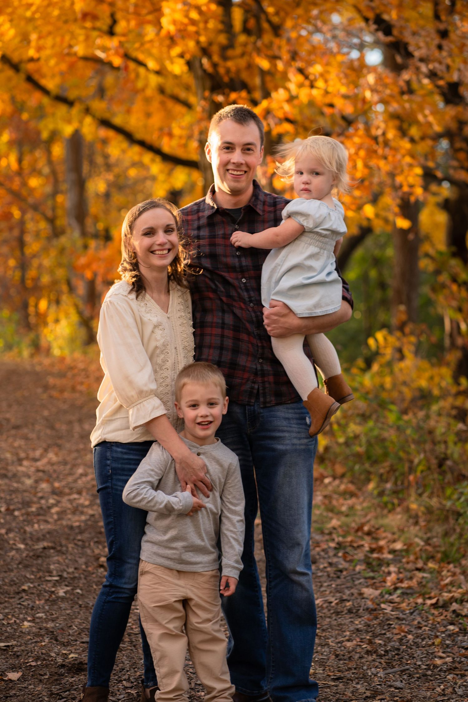 A family stands together on a forest trail surrounded by vibrant autumn foliage in golden yellow and orange hues.