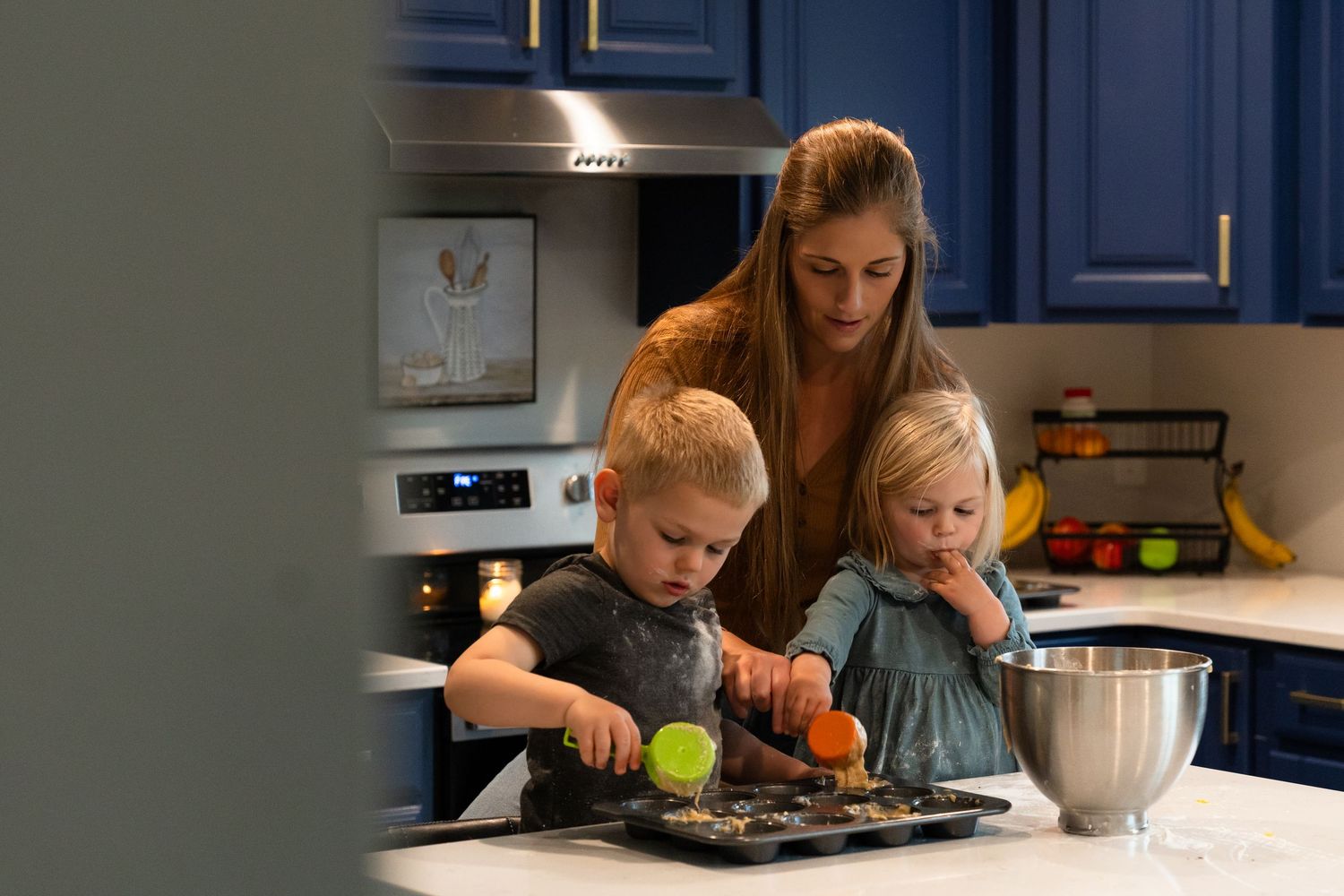 Children helping with baking in a modern blue kitchen while an adult supervises their cooking activity.