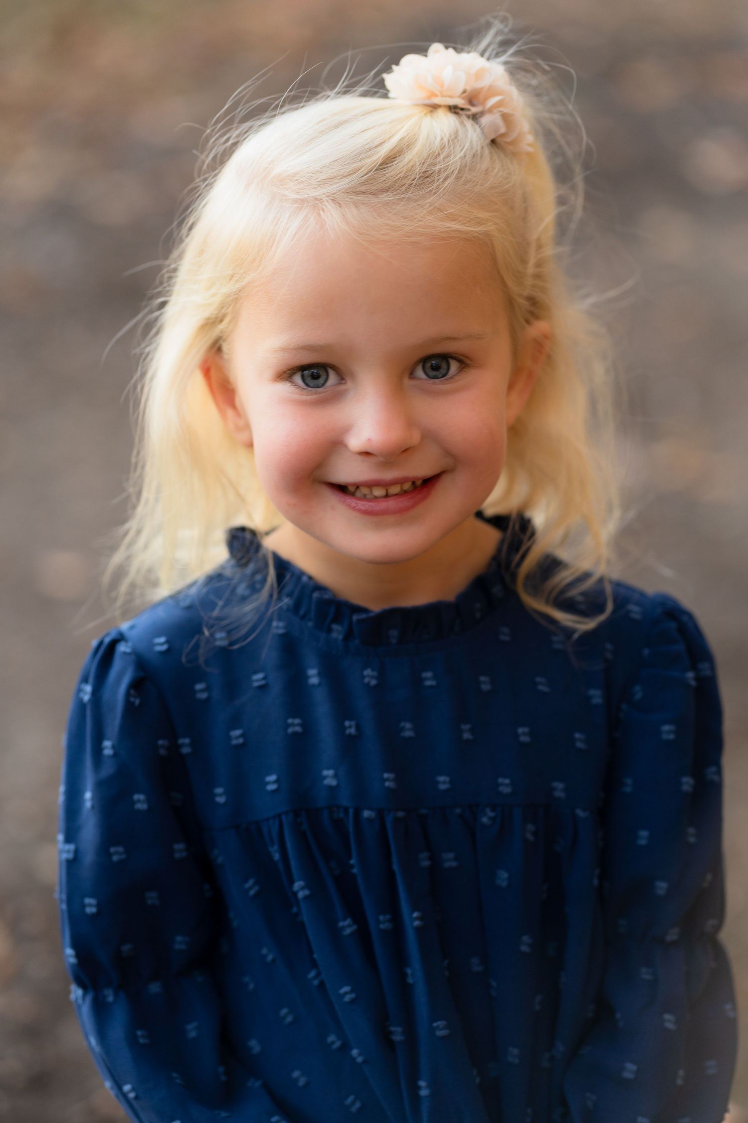 Portrait of a young child with blonde hair in a blue patterned dress smiling warmly at the camera.