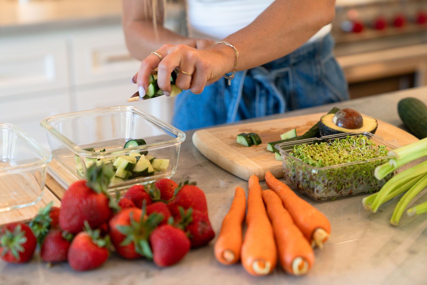 Fresh produce including strawberries, carrots, and avocado being chopped on a wooden cutting board in a kitchen.