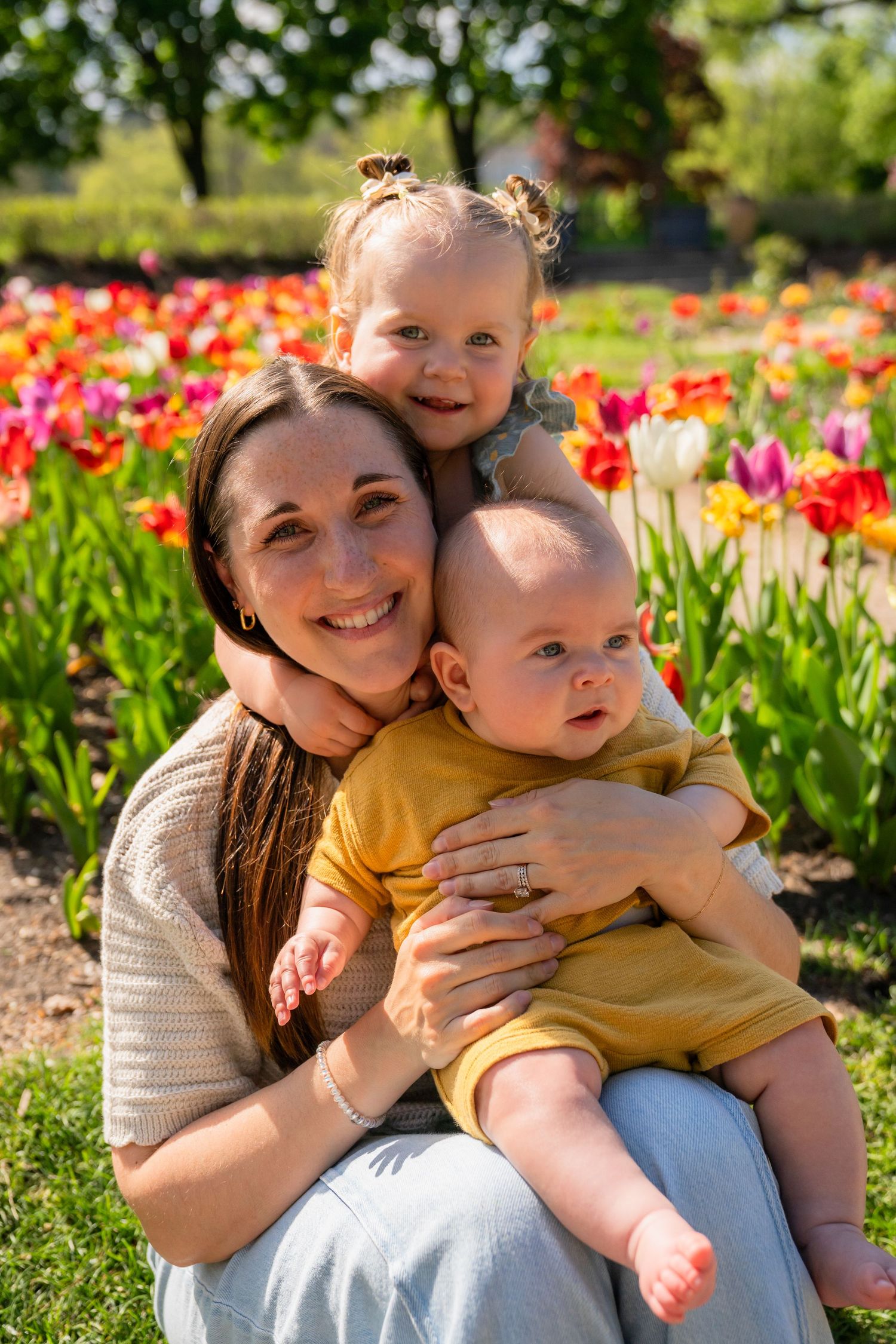 Happy family posing together among vibrant spring tulips in a sunny garden setting.