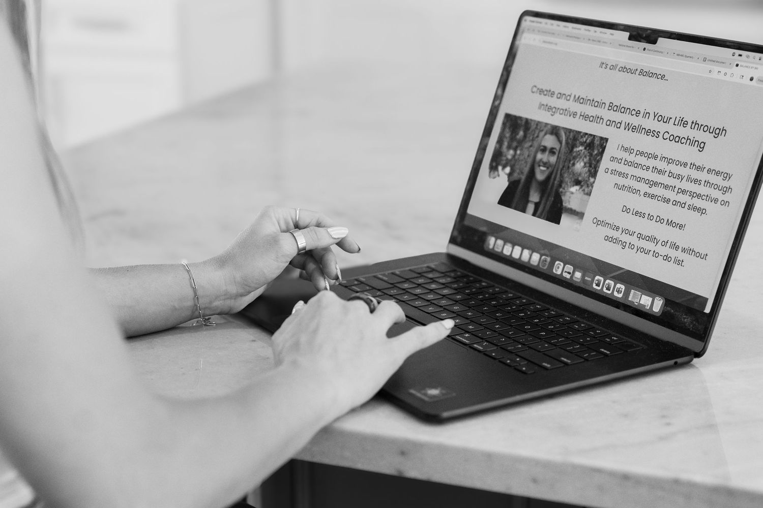 Someone types on a laptop keyboard showing a news article on the screen in black and white.