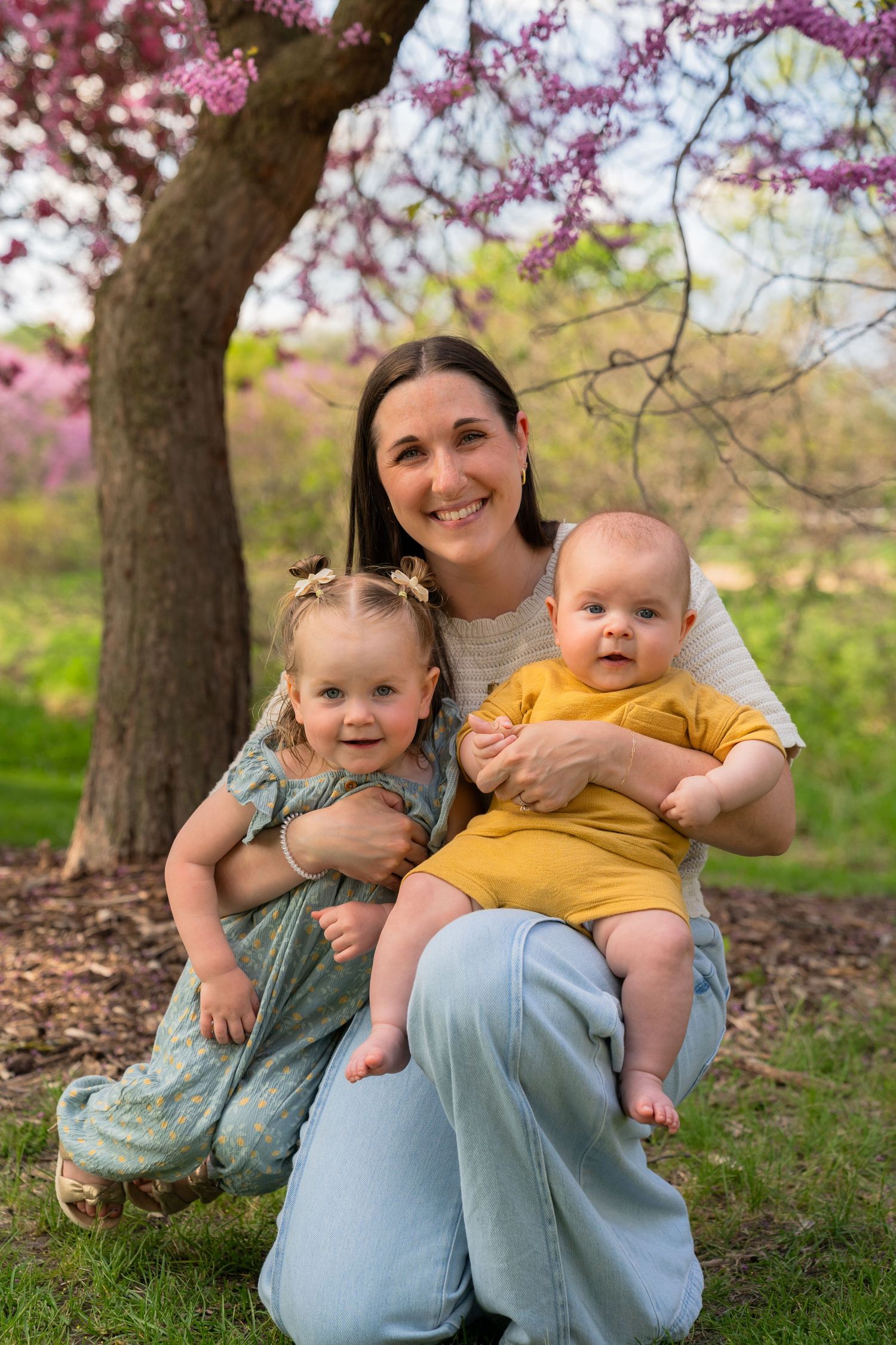 A spring family portrait under a blooming cherry tree with pink blossoms in a park setting.