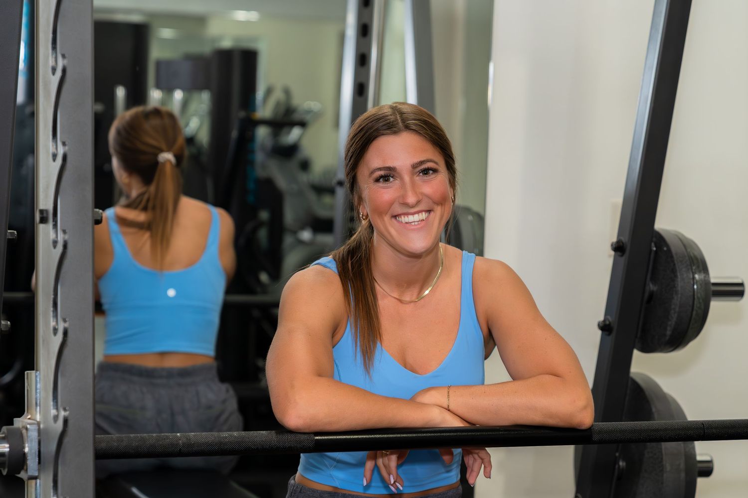 Woman in blue workout tank top performing barbell squat exercise at a well-equipped gym.