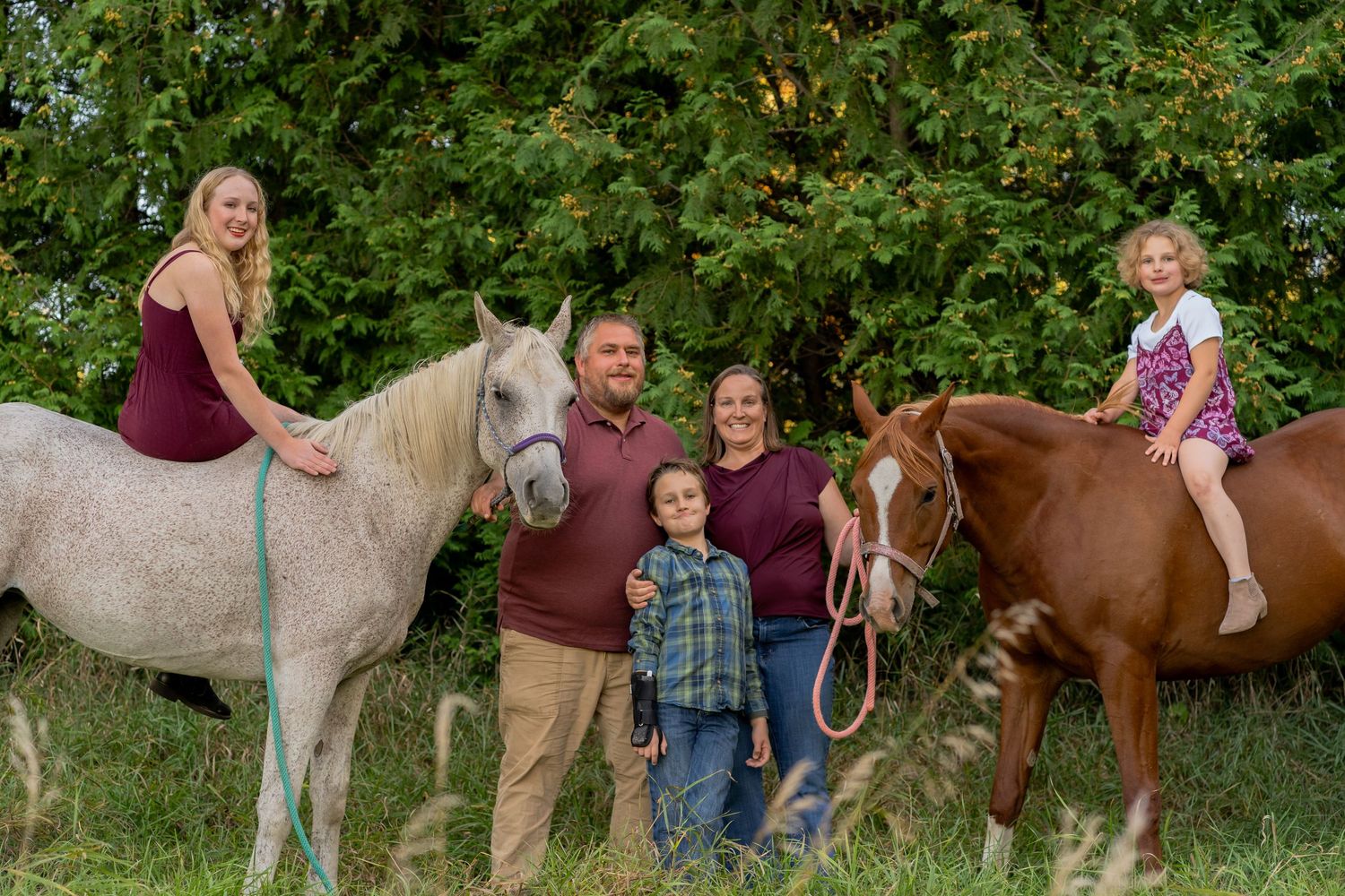 A group outdoors with two horses - a white horse and a brown horse - surrounded by lush green foliage.