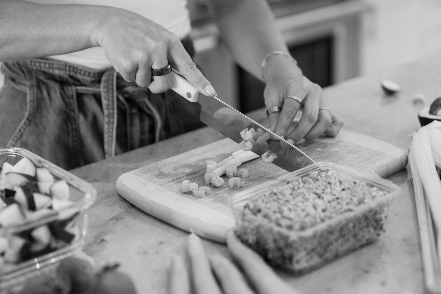 A pair of hands cuts mushrooms on a wooden cutting board in black and white photography.