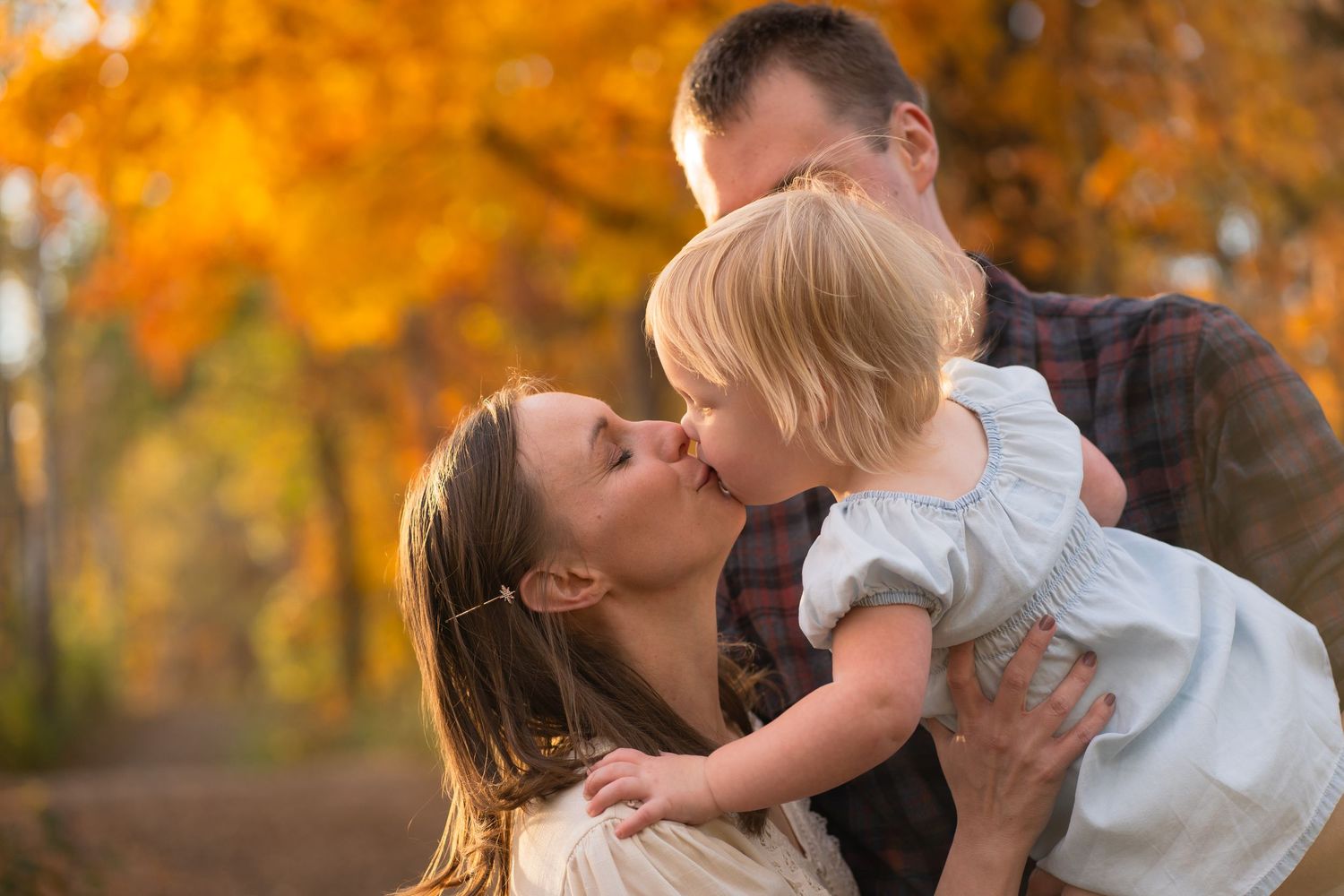 A tender family moment shared between adults and a small child against a backdrop of golden autumn foliage.