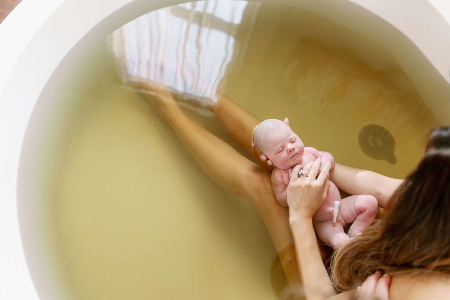 A gentle bath time moment with caregiver and baby in a warm-toned photo taken from above.