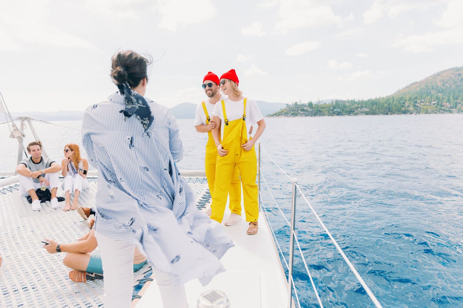 People enjoying a sunny day on a catamaran sailing boat with blue water and mountains in the background.