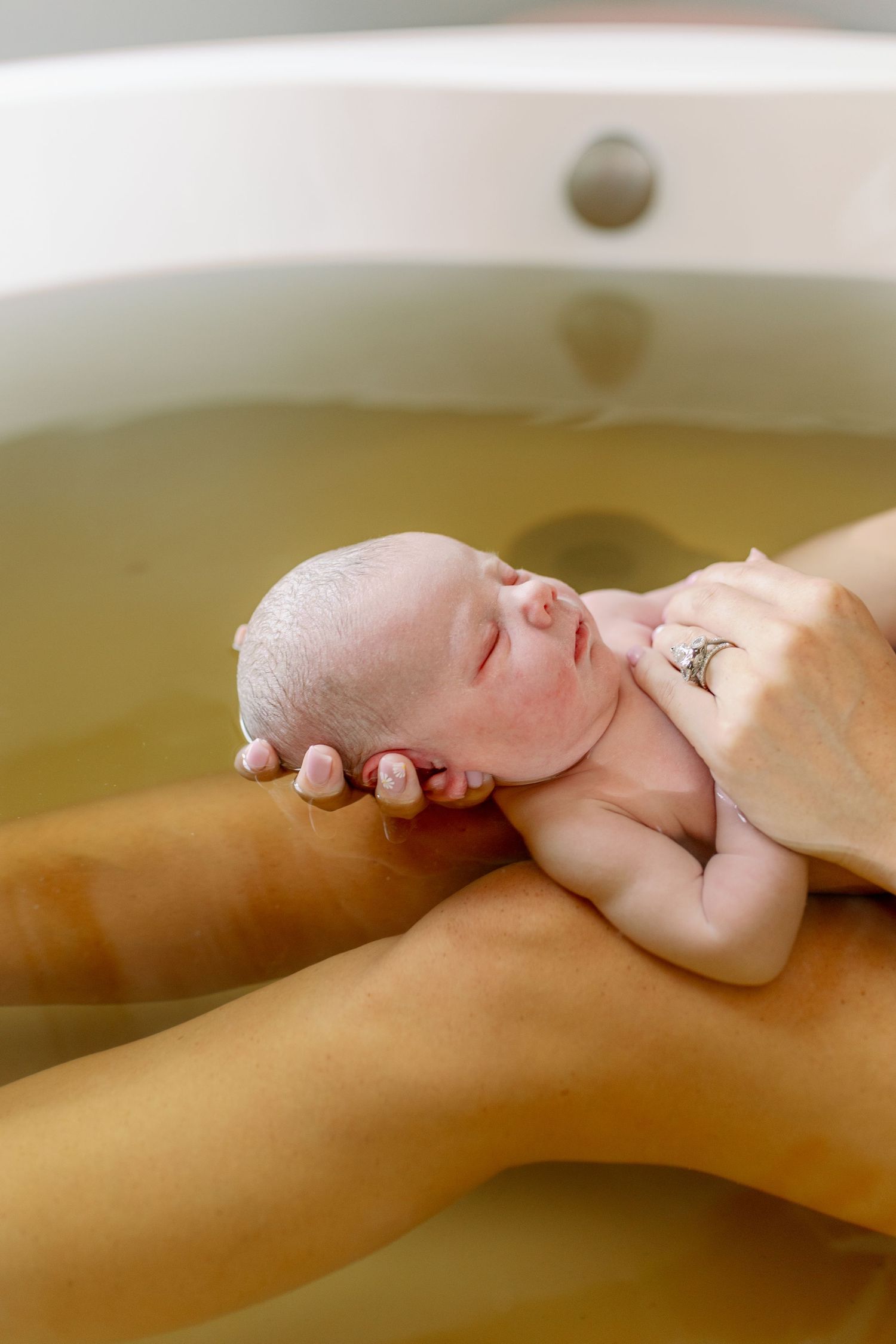 Tiny newborn in gentle hands during warm bath in green tinted water.