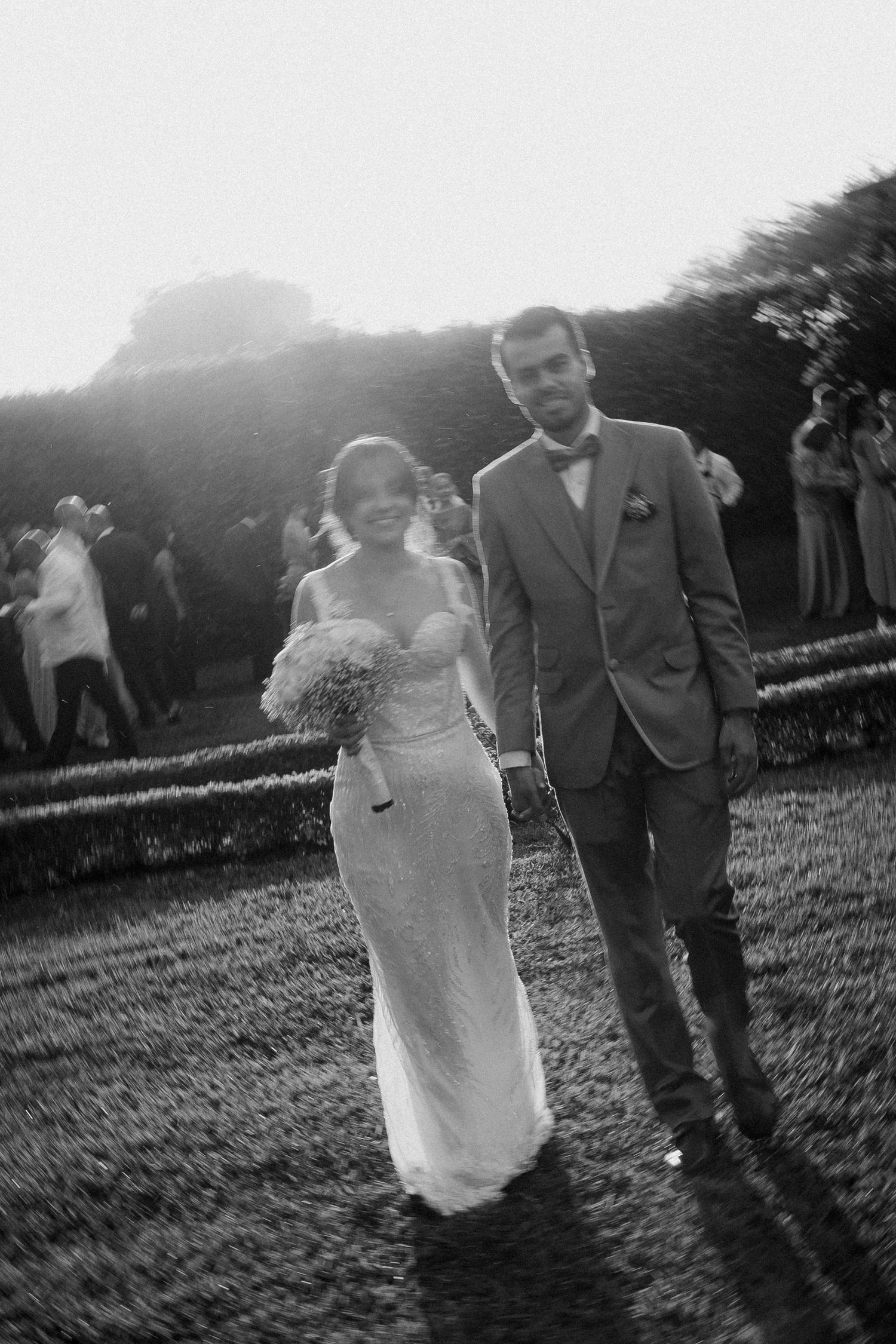 A couple walks together outdoors during their wedding celebration on a grassy lawn at sunset.