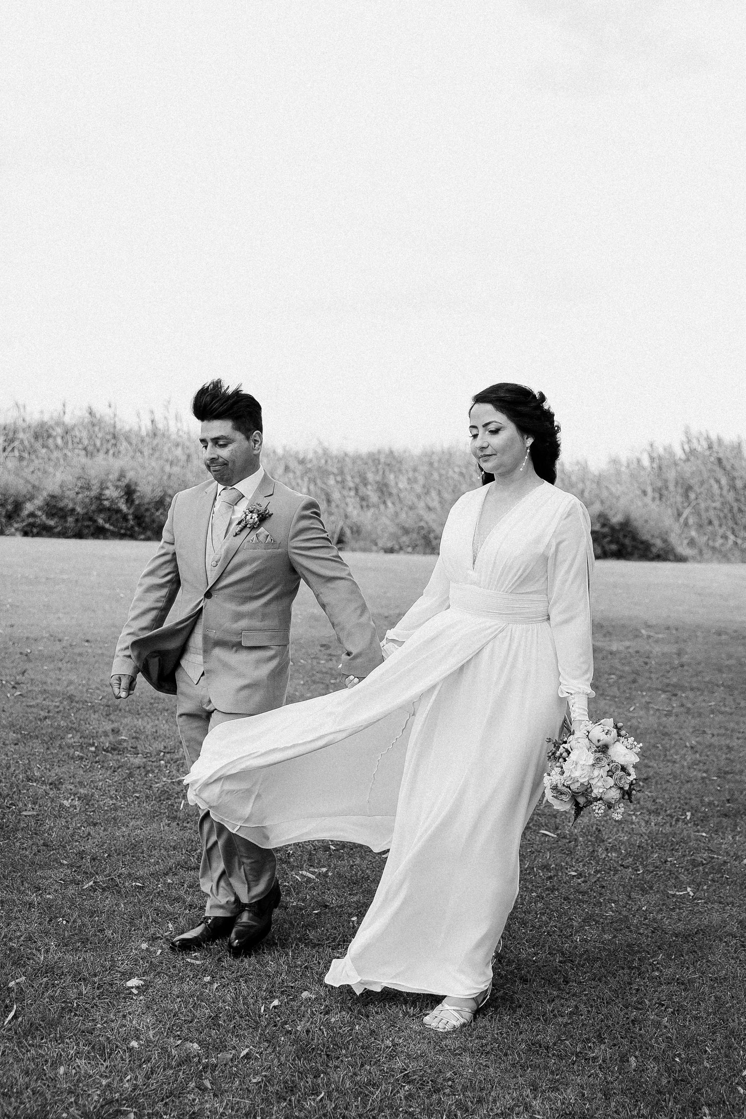 Black and white wedding photo of a couple walking outdoors, with the bride's dress flowing in the wind.