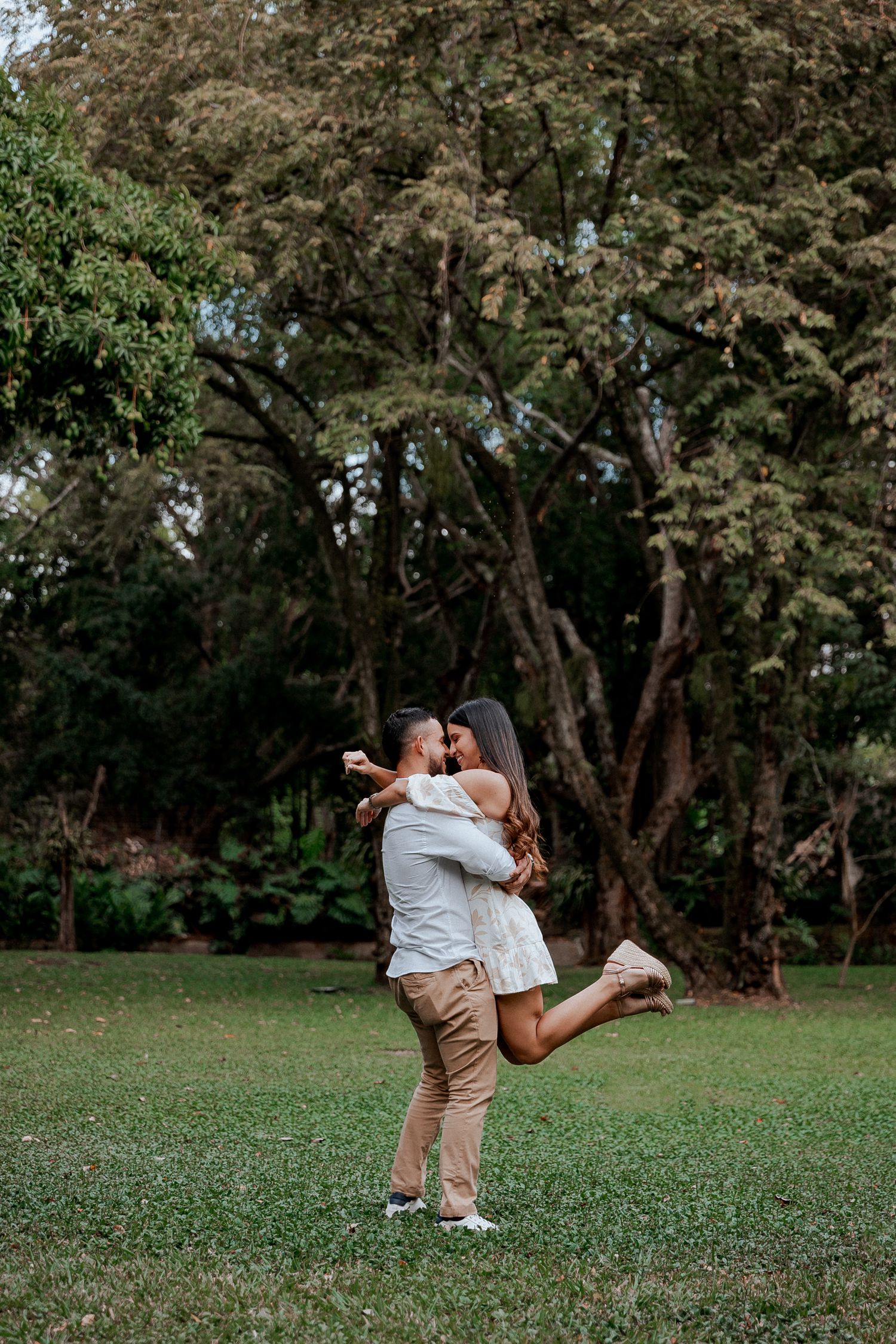 Couple sharing a joyful embrace in a lush garden with blooming trees.