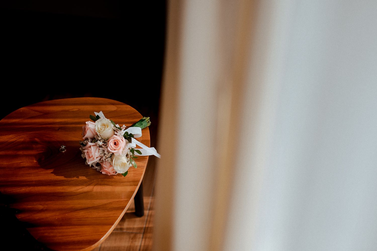 Pink and white floral bouquet rests on the corner of a polished wooden surface with soft window light in background.