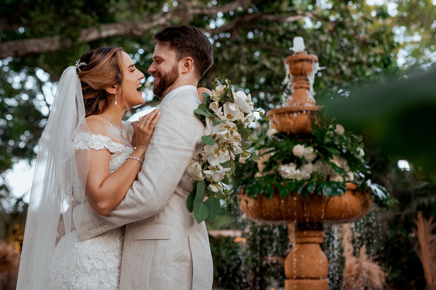 A joyful couple shares a tender moment near an elegant garden fountain during their outdoor wedding celebration.