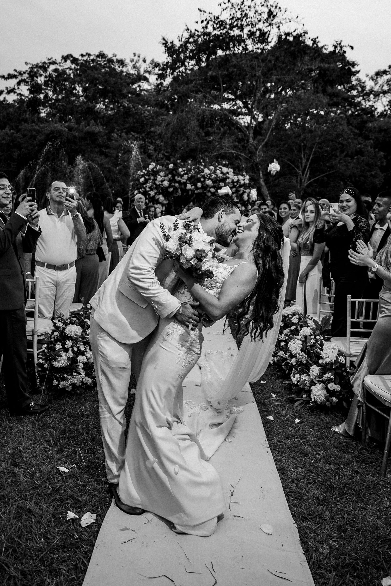 Newlyweds sharing their first dance surrounded by guests at an outdoor garden wedding ceremony.