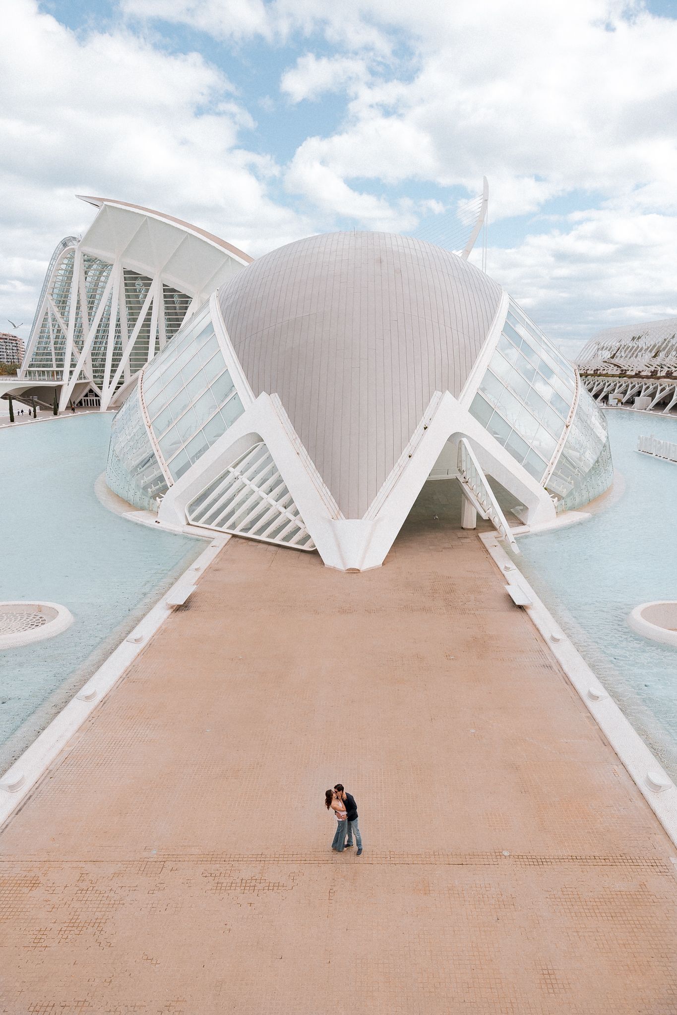 Architectural photo of a modern white building with a dramatic curved design and two figures standing on a pathway.