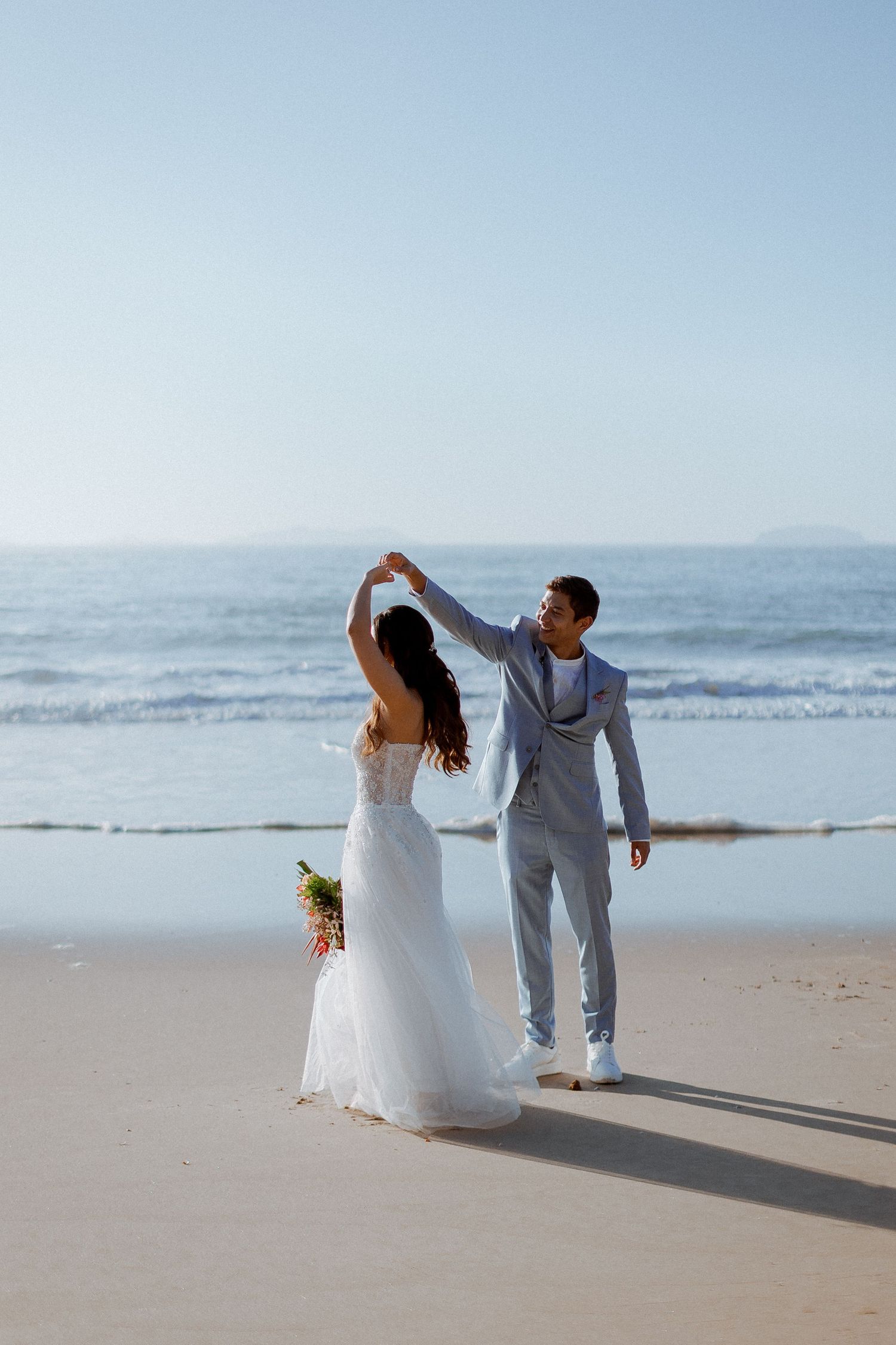 A couple dancing together on a sandy beach at sunset with waves rolling in the background.