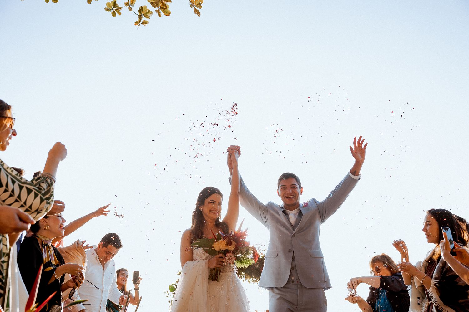 Wedding guests shower happy newlyweds with confetti during joyful outdoor celebration under autumn trees.