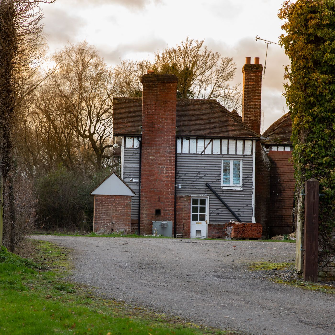 Traditional English countryside house with red brick chimneys, white windows, and gray weatherboarding set on a gravel driveway.
