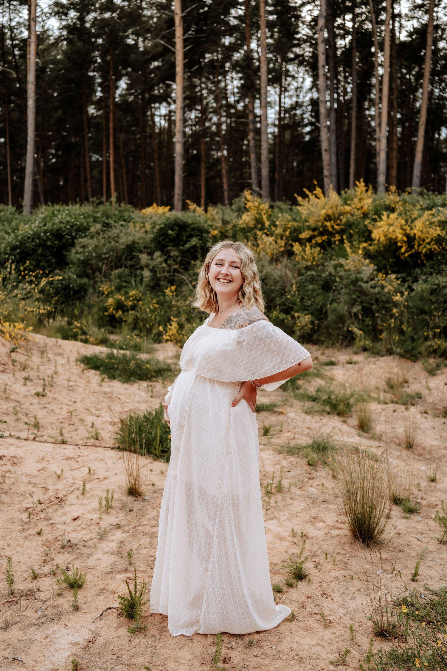 Strahlende Schwangere im weißen Kleid steht lachend in der Natur zwischen Ingolstadt & Nürnberg - authentisches Babybauchshooting.
