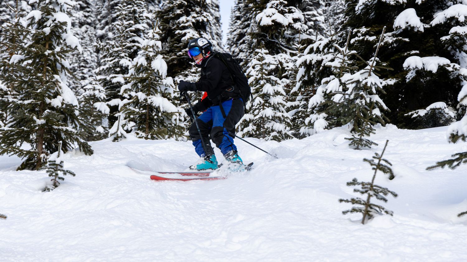 Skier launching off snow with bright red skis against winter forest background.