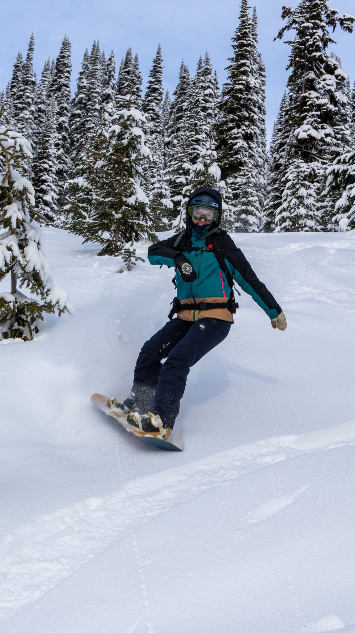 Snowboarder riding down a snowy slope surrounded by frost-covered pine trees.