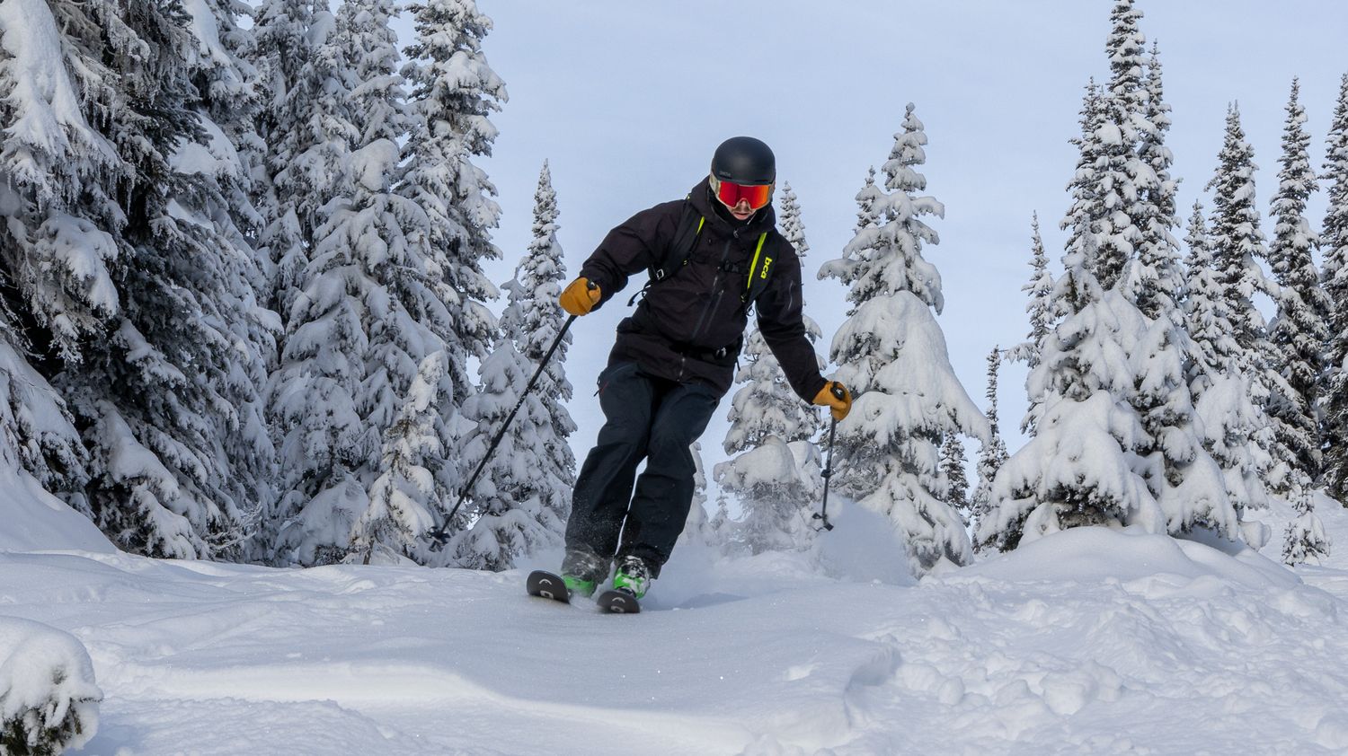 Winter athlete navigating through snowy terrain with snow-covered pine trees in background.