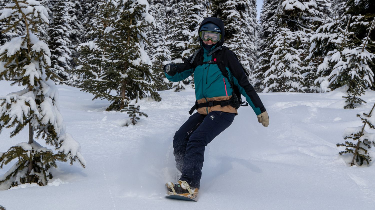 Snowboarder riding through pristine powder snow between snow-covered evergreens.