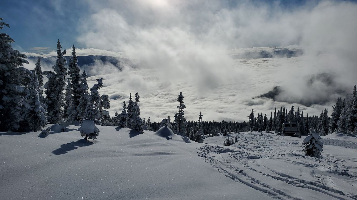 Snow-covered mountain landscape with evergreen trees under dramatic cloudy winter sky.