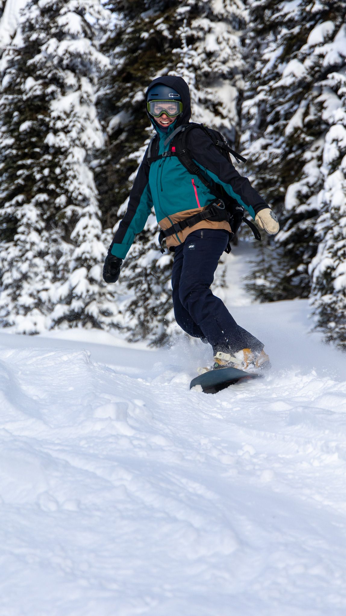 A snowboarder catches air while jumping on a snowy slope surrounded by evergreen trees.