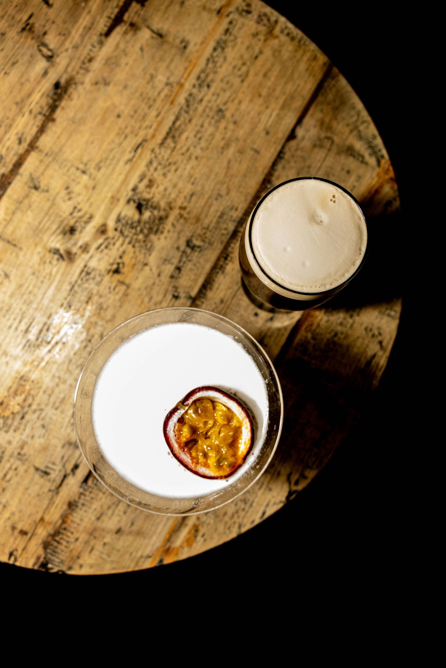 A slice of passion fruit floats in a creamy white cocktail served on a rustic wooden surface with dramatic lighting.