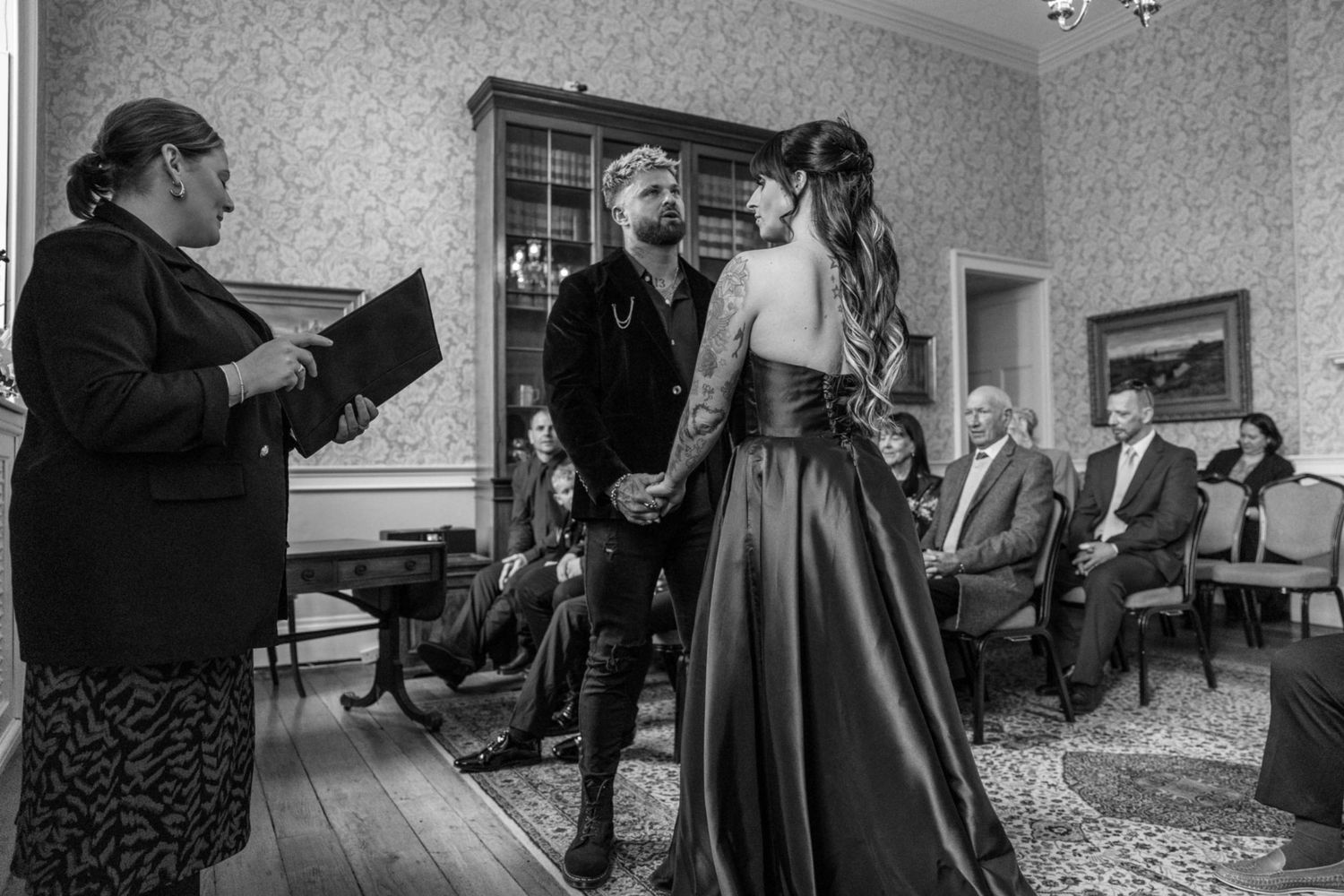 An intimate black and white photo of a civil ceremony taking place in a vintage-style room with ornate decor.