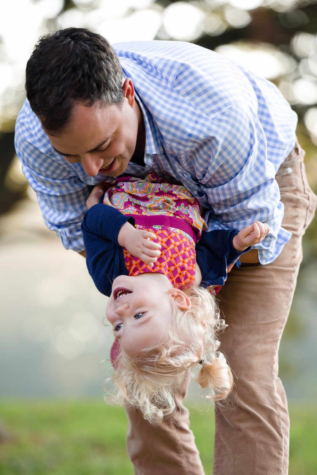 Parent and child share a playful moment outdoors, bending over backwards in matching blue gingham shirts.