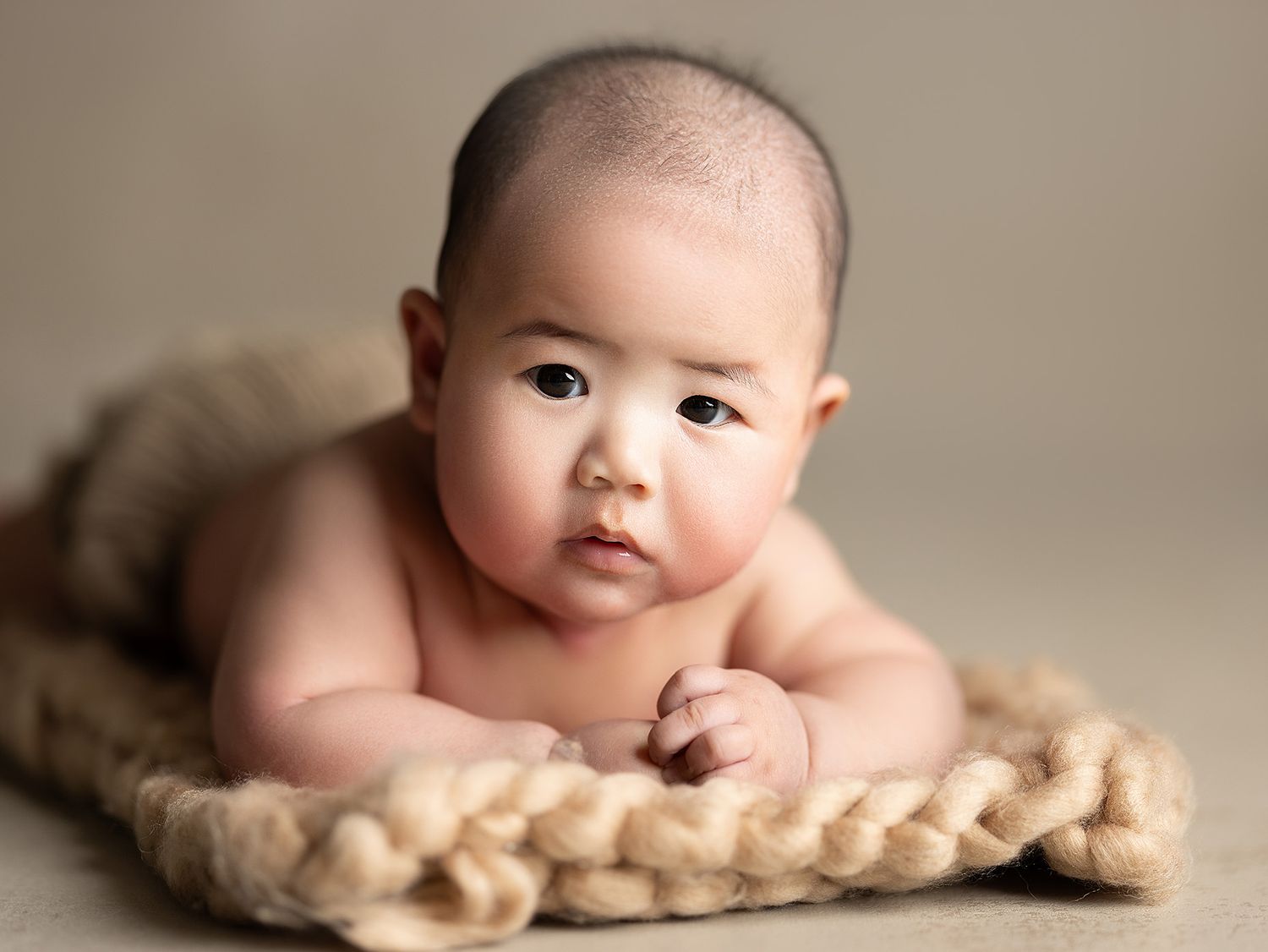 A close-up portrait series of a baby lying on a soft cream-colored blanket showing different expressions and poses.
