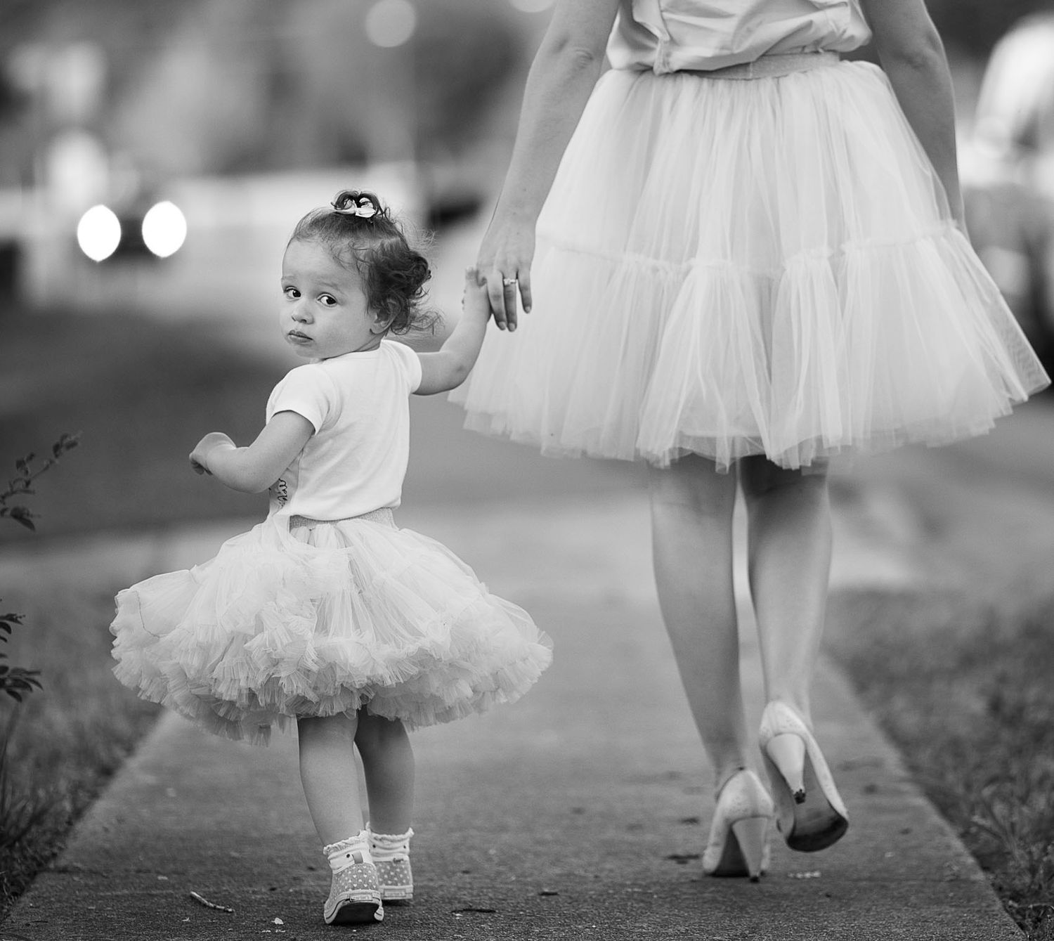 Several small dancers in white tutus practice ballet moves outdoors in a graceful black and white photographic series.