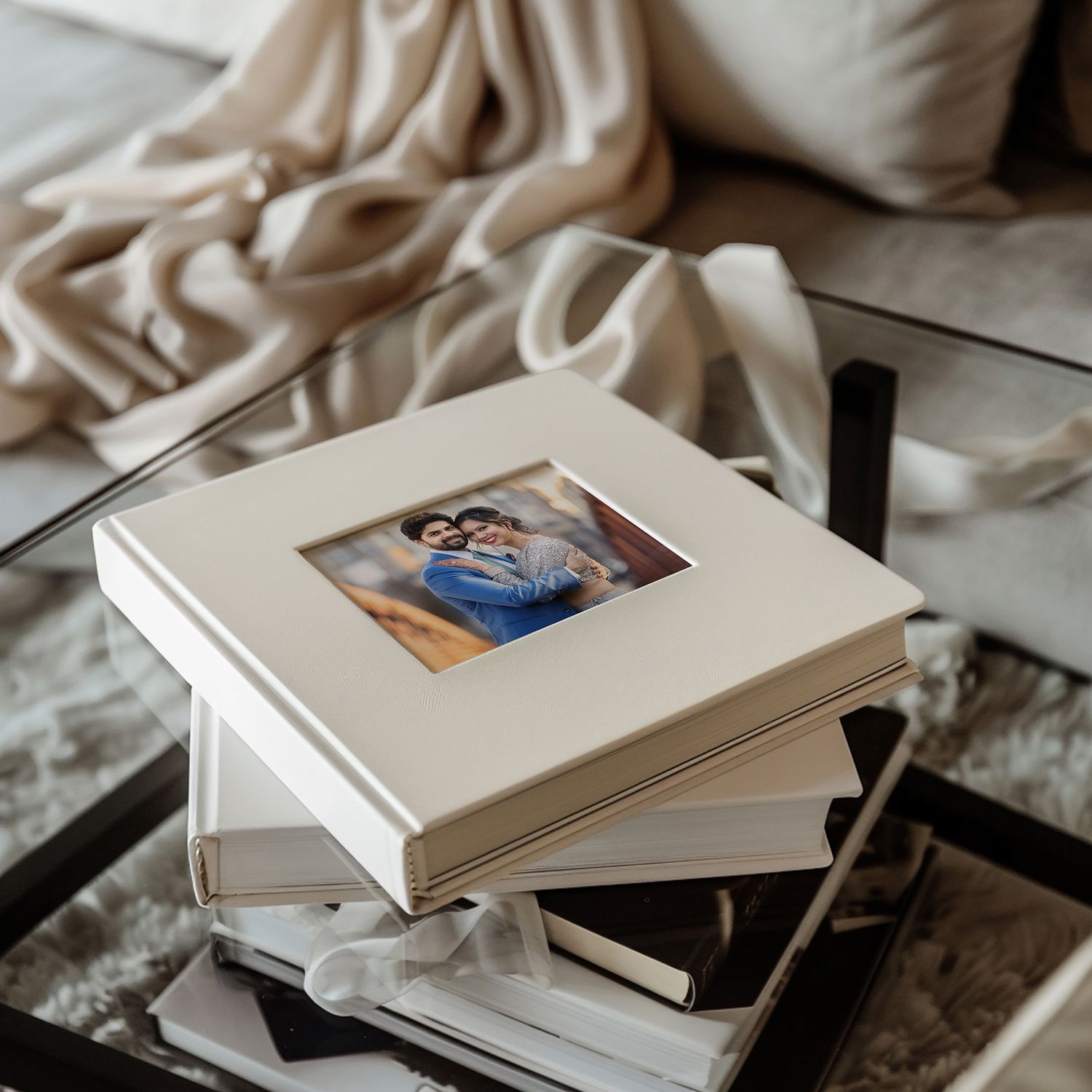 Stack of white hardcover books arranged on a textured cream-colored fabric surface with photo inserts visible.