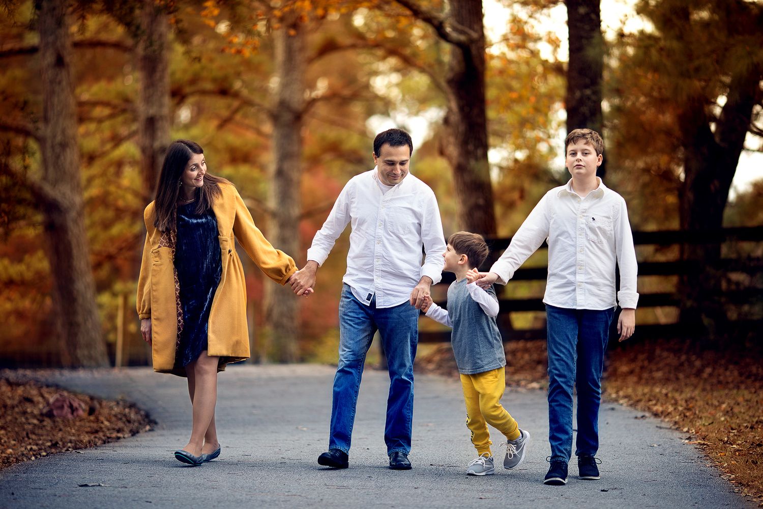 Family of four people enjoying an autumn walk together on a tree-lined path covered in fallen leaves.