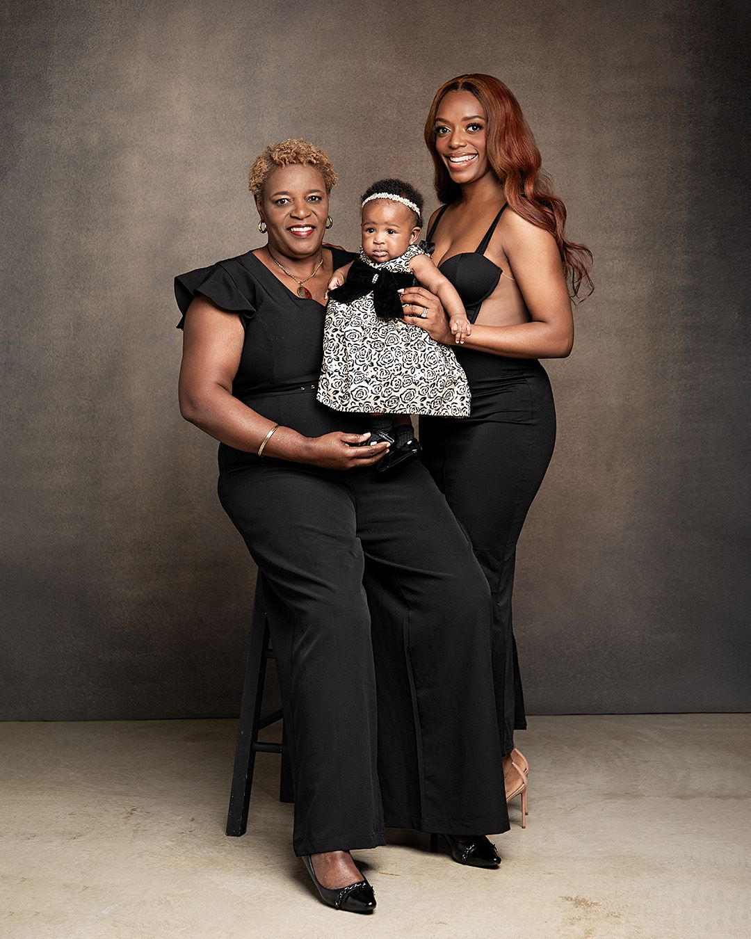 Three generations in a professional studio portrait wearing black outfits against a textured grey background.