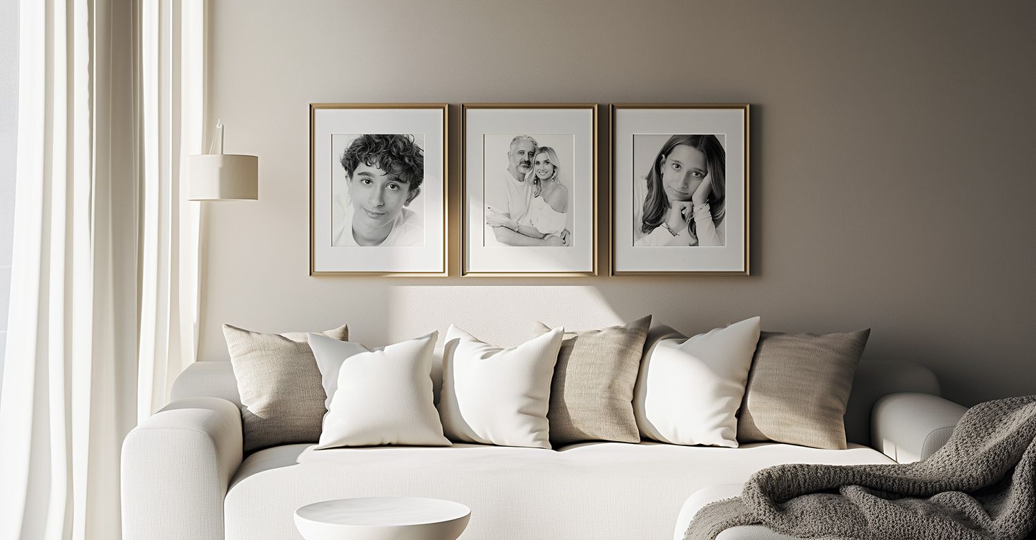 Living room wall with framed portraits above a beige sofa with neutral throw pillows.
