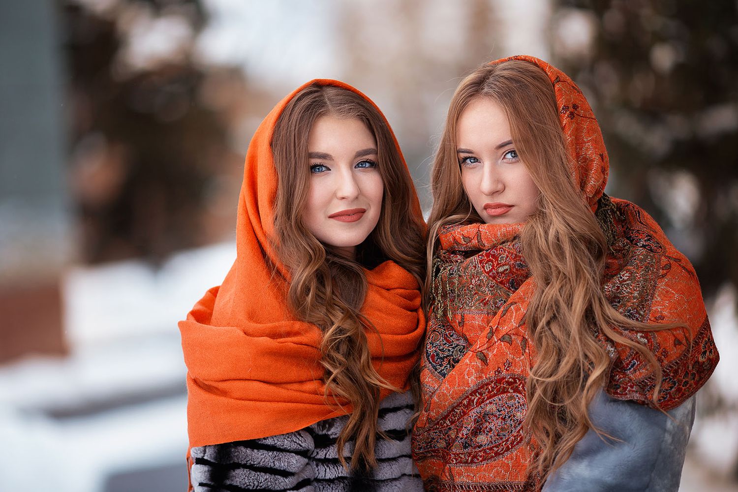 Two people wearing vibrant orange scarves pose together in a snowy winter setting.