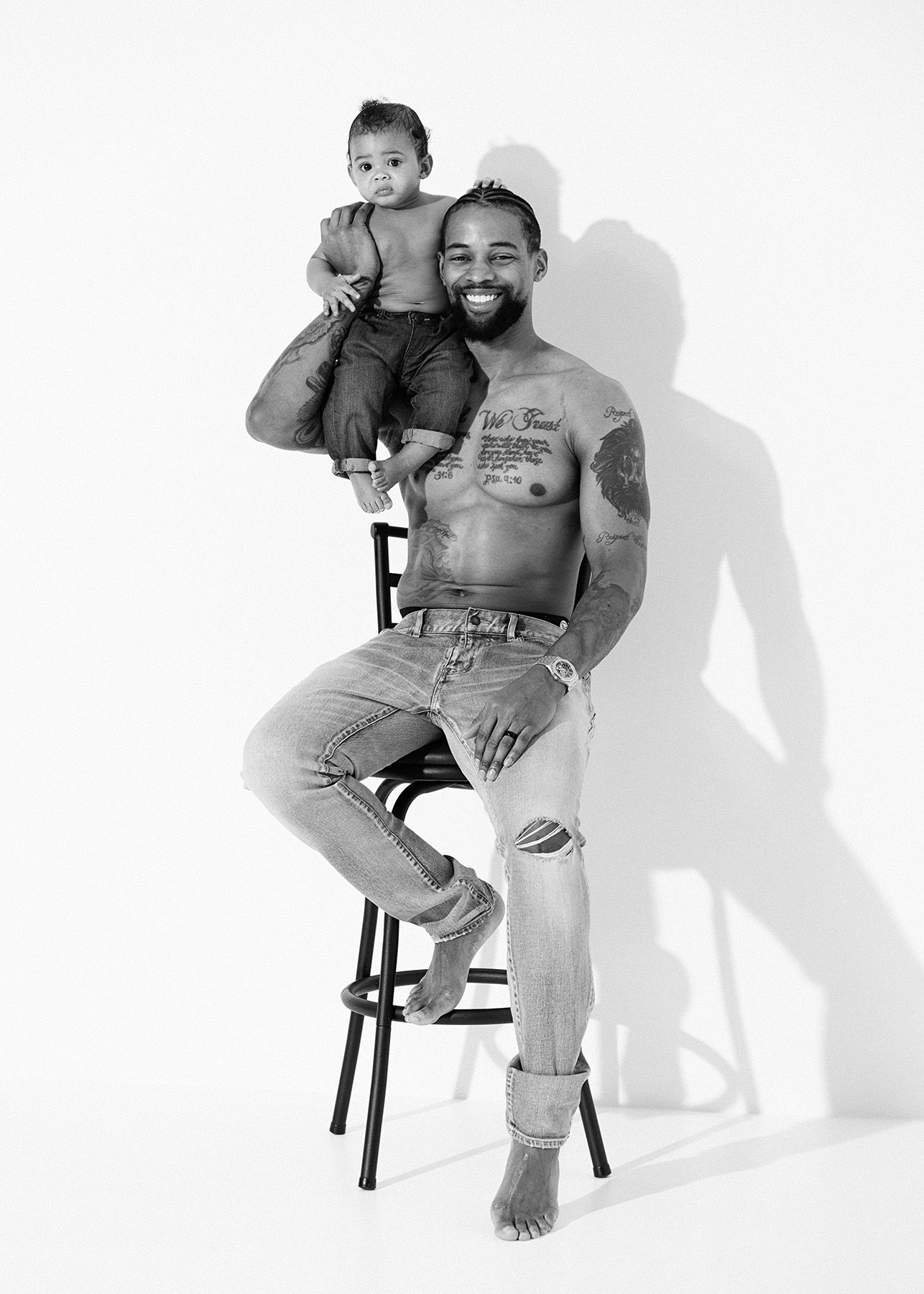 Black and white portrait of a person sitting on a stool with a child on their shoulders against a white backdrop.