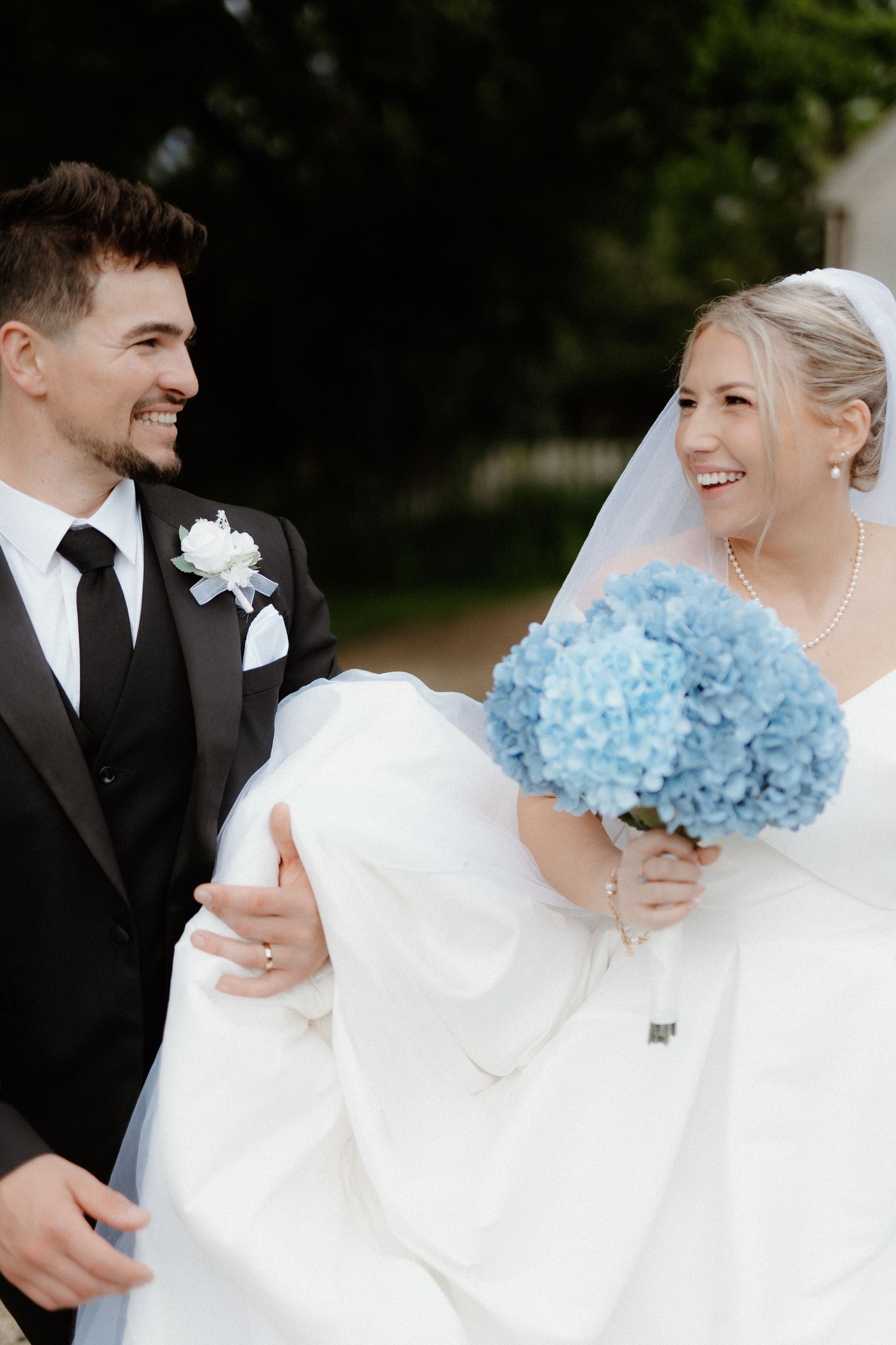 A happy couple shares a joyful moment on their wedding day with a beautiful blue hydrangea bouquet.