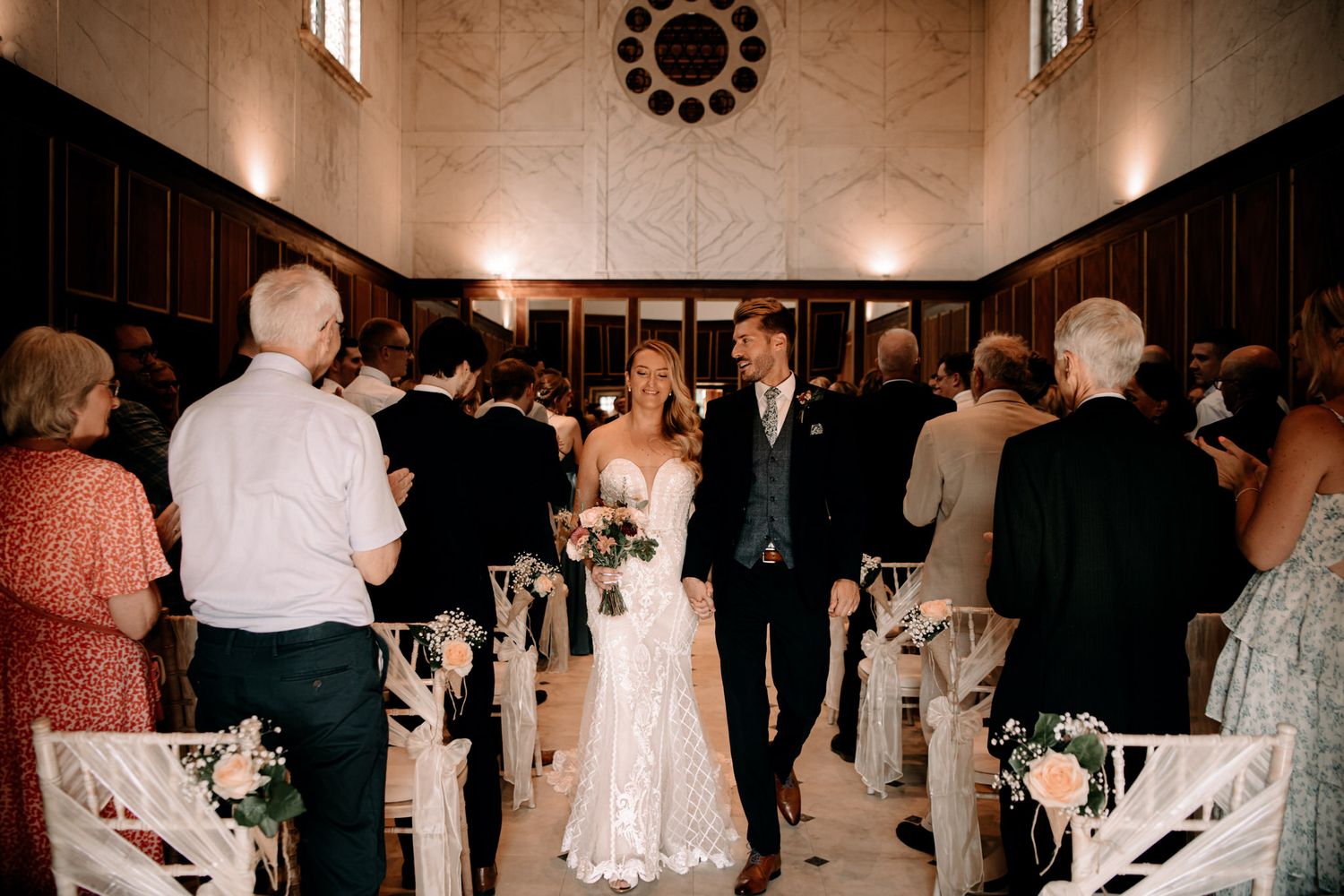 A wedding ceremony inside a historic church with high ceilings and elegant decor featuring white floral arrangements along the aisle.