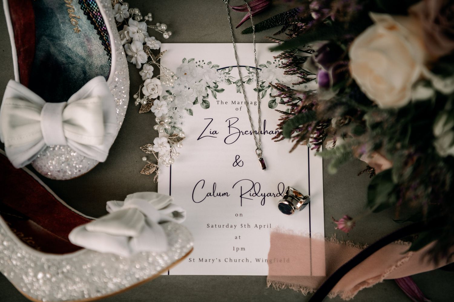 Elegant wedding invitation with white bow shoes and roses on dark wooden surface with delicate floral accents.